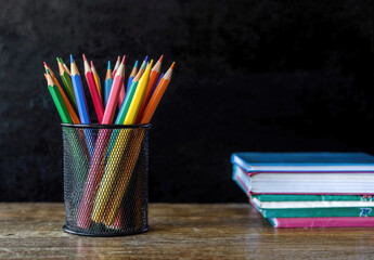 Aufkleber - Colorful pencils is standing in a metal pencil holder on a wooden desk with books and a blackboard in the background