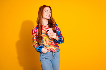 Wall Mural - Photo of positive girl with foxy hair dressed print shirt hold smartphone look at sale empty space isolated on yellow color background