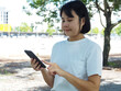 © MarutStudio - Asian woman tourist or business woman relaxing walking in park under big green tree using smart phone surfing internet; texting and communicating outdoors. Weekend leisure lifestyle.