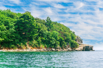 Wall Mural - scenic summer landscape of beautiful sea shore with water vawes in bay, green forest on isle rock and nice cloudy sky on background