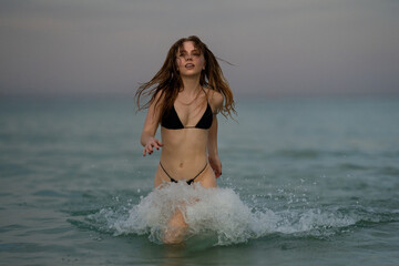 Outdoor fashion portrait of sexy fit tan perfect woman in sexy bikini swim in the sea. Summer mood. Beach trendy swimsuit. Summer girl running and splashing in sea water. Sexy body.