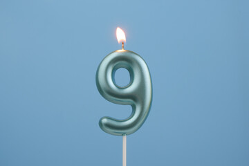 Burning blue birthday candle on blue background, number 9