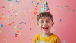 © VK Studio - A boy in a party hat laughs joyfully amid floating colorful confetti, celebrating with enthusiasm against a cheerful pink backdrop.