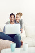 © SunriseDon/peopleimages.com - Happy couple, ecommerce or laptop for option, reading news or movie streaming online on sofa in living room. Relax, internet or people on social network app on digital website or technology in home