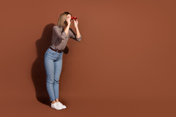 Canvas Print - Photo of glad cheerful woman wear checkered stylish clothes hand hold binoculars look empty space isolated on brown color background