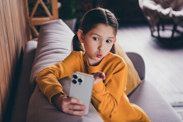 Wall Mural - Photo portrait of nice little girl sit couch send air kiss selfie photo wear orange clothes modern interior flat indoors