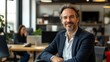 © El Media - Portrait of a business man sitting in an office with his colleagues in the background. Happy business man working in a co-working office. Generative ai