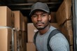 © Milos - A focused young man wearing a cap and backpack is surrounded by stacked brown boxes, representing hard work and determination in a warehouse or delivery setting.