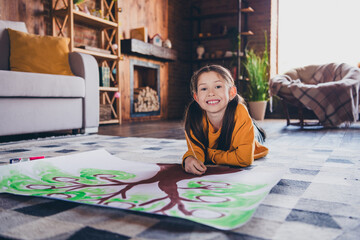 Wall Mural - Full body photo of nice little girl lying floor drawing family tree homework wear orange clothes modern interior flat indoors