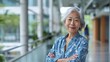 © Sirichat. Camphol - A warm-looking older Asian woman wearing casual clothes, crossing her arms, posing in a friendly manner, and looking at the camera with a sense of success and self-confidence.