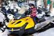 © Studio Peace - Row of snowmobiles stands on the snow at edge of the forest. Little girl is sitting on a snowmobile.