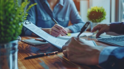 Poster - Two individuals engage in a productive discussion at a desk filled with documents and laptops, surrounded by vibrant greenery