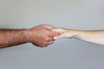 Male hand holding female hand on a grey background. Love, trust, care, relationships, help, friendship between a man and a woman. Handover, handshake