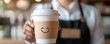 © Nattapun - A close-up of a smiling barista handing a coffee cup with a cute message written on the sleeve