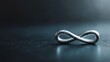 © Dulemegapixel - A close-up view of a silver infinity symbol laying on a dark, reflective surface suggesting the eternal or infinite concept. The background is out of focus.