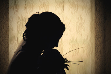 Silhouette of a bride in profile with a bouquet of flowers against a window