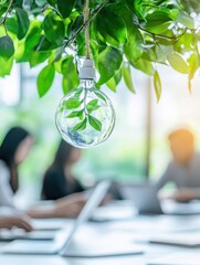 Aufkleber - Close-up of a light bulb with a plant inside, hanging in an office setting with people working on laptops in the background.