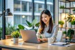© Sirinporn - A cheerful Asian female employee sits at her desk in a modern corporate office, working on her laptop with a smile, surrounded by sleek decor.
