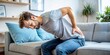 © Sirinporn - A tired young adult suffering from back pain after a nap on the couch, massages their lower back with both hands, highlighting poor posture issues.