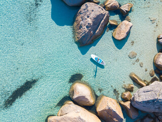 Top down view of young woman enjoying stand up paddleboarding over turquoise water. Paradise coastline in the Mediterranean. Active summer vacation concept.