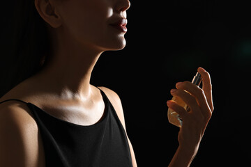 Wall Mural - Woman spraying perfume on black background, closeup