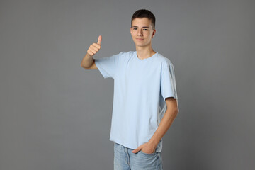 Poster - Teenage boy wearing light blue t-shirt and showing thumbs up on grey background