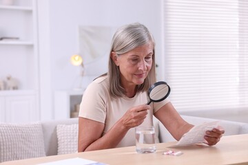 Wall Mural - Senior woman with magnifying glass reading medicine instruction at table indoors