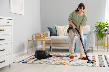 Canvas Print - Young woman cleaning carpet with vacuum in living room