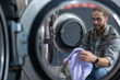 © zinkevych - Caucasian man operating washing machine at commercial laundry