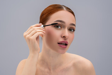 pretty red-haired girl using brush to apply mascara