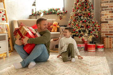 Funny happy dad and little son have fun at home and share Christmas gifts under Christmas Xmas Tree on Merry Christmas Eve in living room at home. Happy New Year