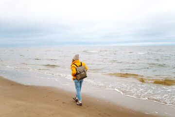 Wall Mural - Back view of  woman tourist walking beach on cloudy day. Cold weather. Calmness and tranquility. Travel, tourism concept.