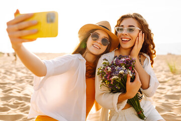 Wall Mural - Two pretty best friends women making selfie on beach, light and bright summer colors. Friends together. Travel, blogging, weekend, relax and lifestyle concept.