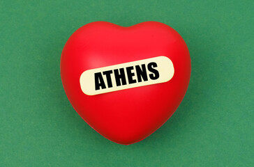 A vibrant red heart symbolizing love for the capital city of Athens adorned with a label, against a green backdrop