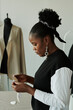 © pressmaster - Side view of young serious African American female fashion designer with stylish earrings holding sewing paper patterns during work
