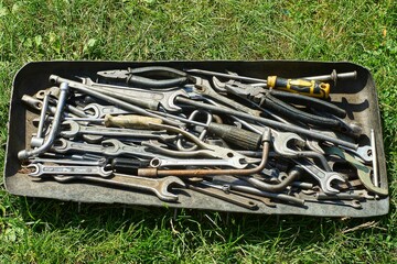 set of different iron gray dirty industrial old wrenches for transport with pliers and screwdrivers lie in tool box on green grass