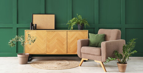 Poster - Interior of living room with armchair, cushion and chest of drawers near green wall