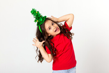 Wall Mural - Little brunette girl in in the rim of a Christmas tree on her head having fun on white background. space for text. the concept of Christmas, joyful at the New Year's party.