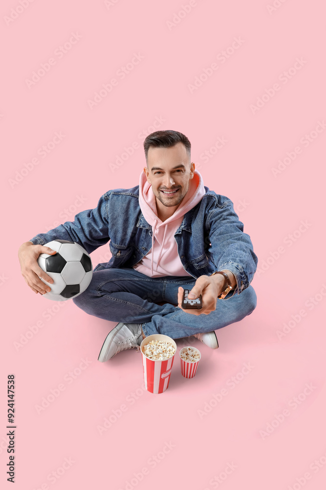 Happy young man with popcorn watching football game on pink background