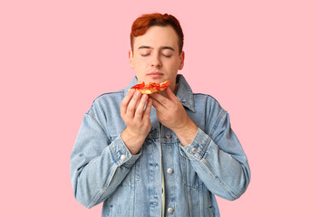 Sticker - Young man eating piece of tasty pizza on pink background