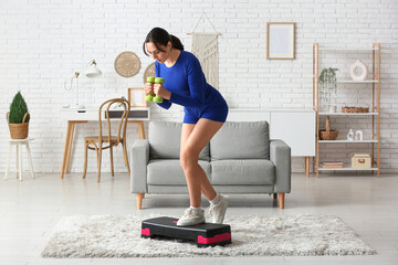 Canvas Print - Sporty young woman training with dumbbells and stepper at home