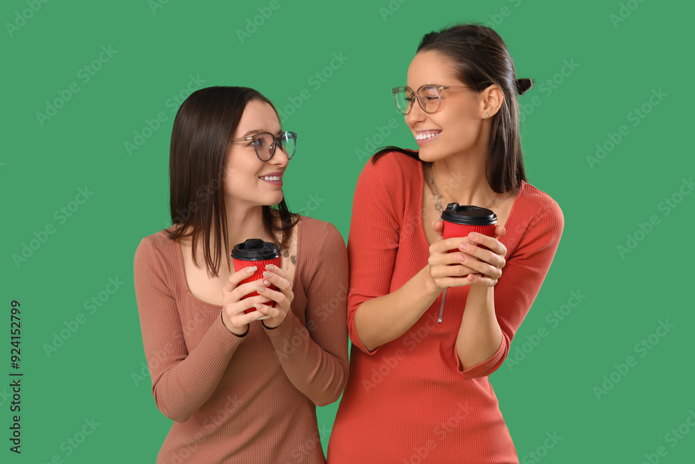 Young women in eyeglasses with coffee cups on green background