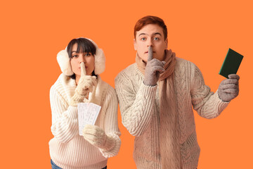 Sticker - Beautiful young couple with passport and tickets showing silent gesture on orange background. Winter vacation concept