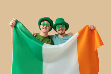 Canvas Print - Happy young men in leprechaun's hats and party glasses with flag of Ireland on beige background. St. Patrick's Day celebration