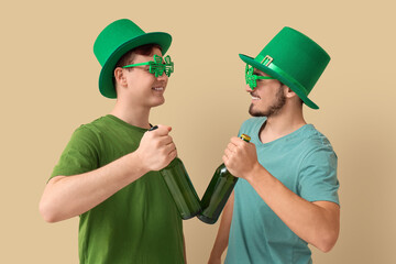 Wall Mural - Happy young men in leprechaun's hats and party glasses with bottles of beer on beige background. St. Patrick's Day celebration