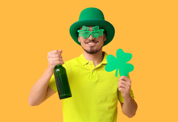 Wall Mural - Happy young man in leprechaun's hat with mug of beer and clover on yellow background. St. Patrick's Day celebration