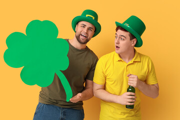 Wall Mural - Young men in leprechaun's hats with bottle of beer and clover on yellow background. St. Patrick's Day celebration