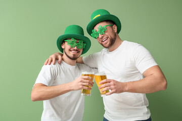 Wall Mural - Happy young men in leprechaun's hats with glasses of beer hugging on green background. St. Patrick's Day celebration