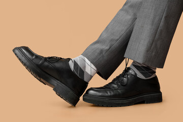 Wall Mural - Legs of young man in black elegant shoes on brown background