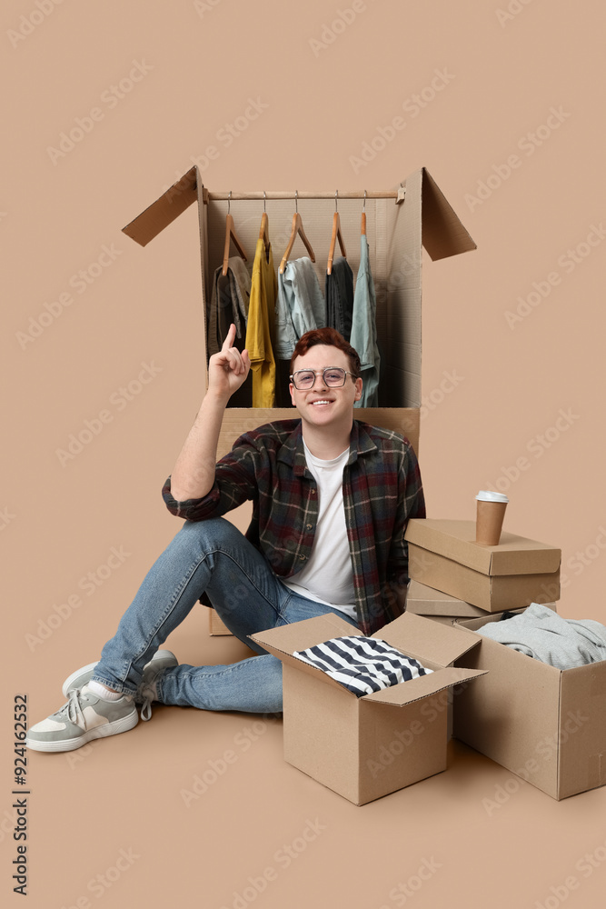 Happy young man sitting near wardrobe boxes with clothes on beige background